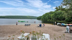 A lakeside beach with lounge chairs and a green inflatable raft.