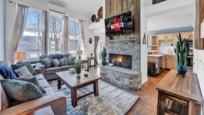 A cozy living room with a stone fireplace, a flat-screen TV mounted above it, and a comfortable seating area with a sofa and a coffee table.
