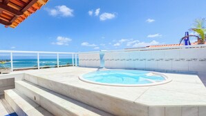 Una piscina en la azotea con vista al océano, rodeada por una barandilla blanca y escalones que bajan a la piscina.
