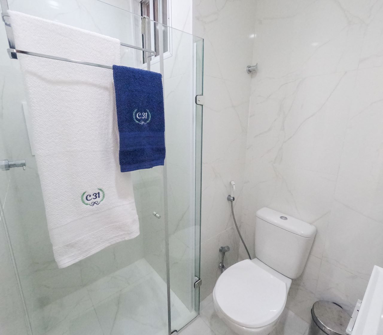 Een moderne badkamer met een douchecabine van glas, een wit toilet en twee handdoeken aan een glazen handdoekenhouder.