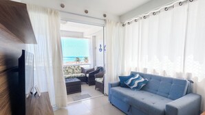 Una sala de estar con un sofá azul, un televisor y vista a la playa a través de un ventanal.