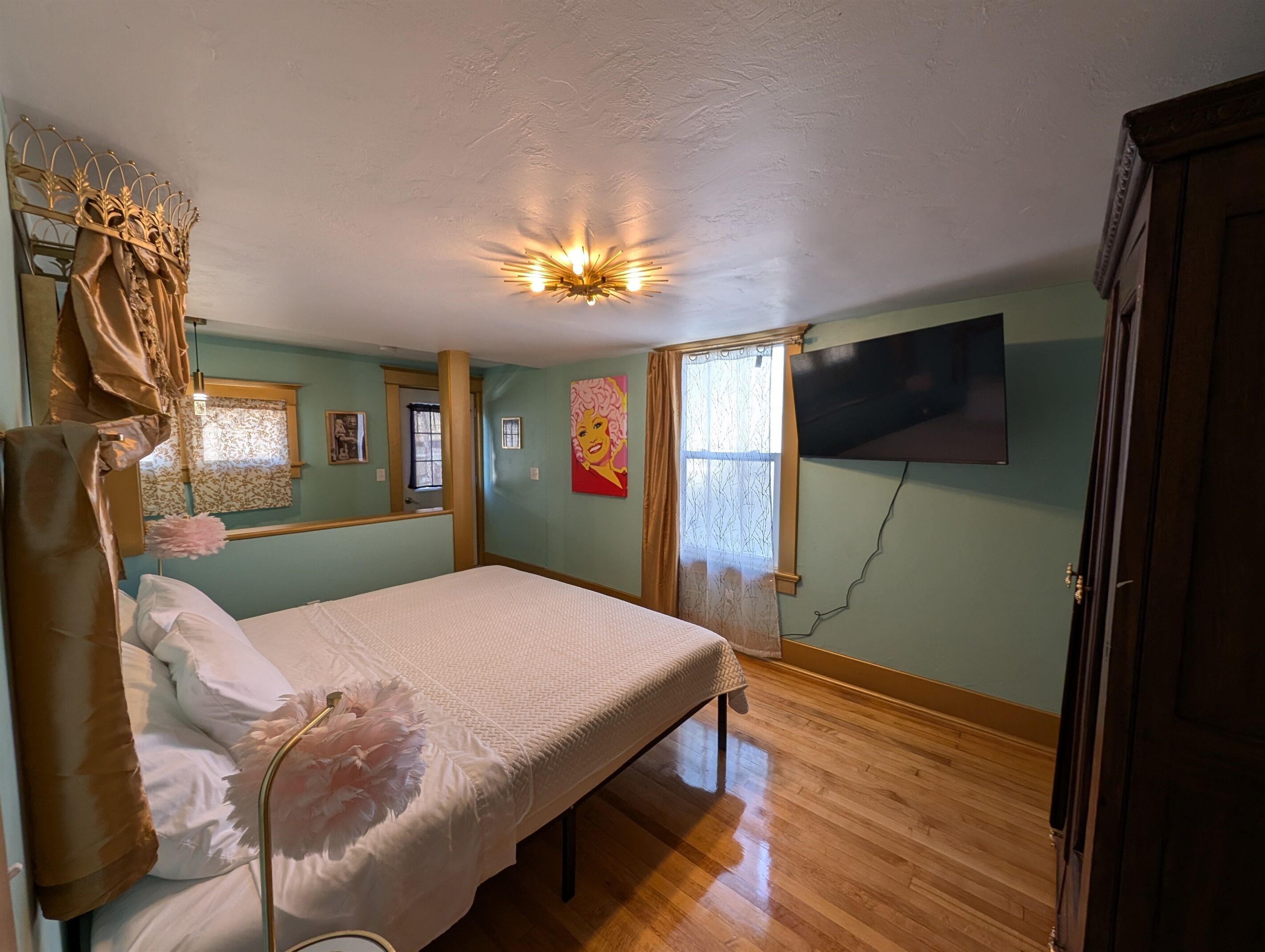 A bedroom with a bed, a ceiling light, a TV, and a window with curtains.