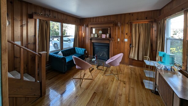 Une pièce chaleureuse avec une cheminée, des murs en bois, un canapé bleu et un fauteuil rose.