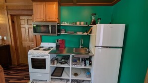 Una cocina compacta con estufa, microondas y refrigerador, armarios de madera y pared verde.