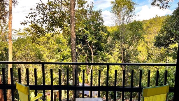 Eine Terrasse mit zwei gelben Klappstühlen und einem kleinen Tisch, umgeben von einem schwarzen Geländer, mit Blick auf eine üppige grüne Landschaft.