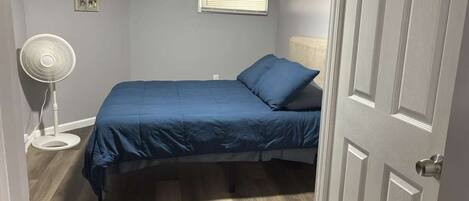 A bedroom with a bed, a standing fan, and a door.