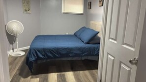 A bedroom with a bed, a standing fan, and a door. - Standard Room G | Near Prudential, EWR & NYC (Newark)