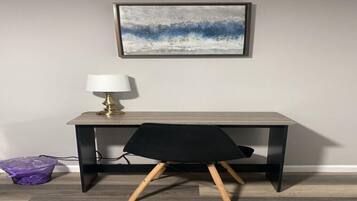 A desk with a lamp, a chair, and a framed artwork on the wall.