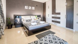 Quarto moderno com cama, mesas de cabeceira, ventoinha no teto e armários embutidos.