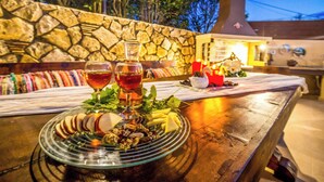 Uma mesa de jantar com um prato de comida e bebidas de vidro, com uma parede de pedra e um banco de madeira ao fundo.