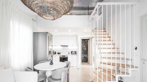 Een moderne keuken met witte kasten, een eethoek met een ronde tafel en stoelen, en een trap met houten treden en witte leuningen.