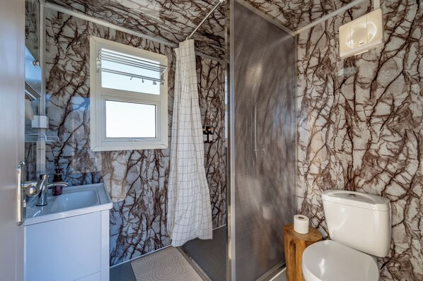 Un baño con pared de mármol, ventana, lavamanos, inodoro y ducha.