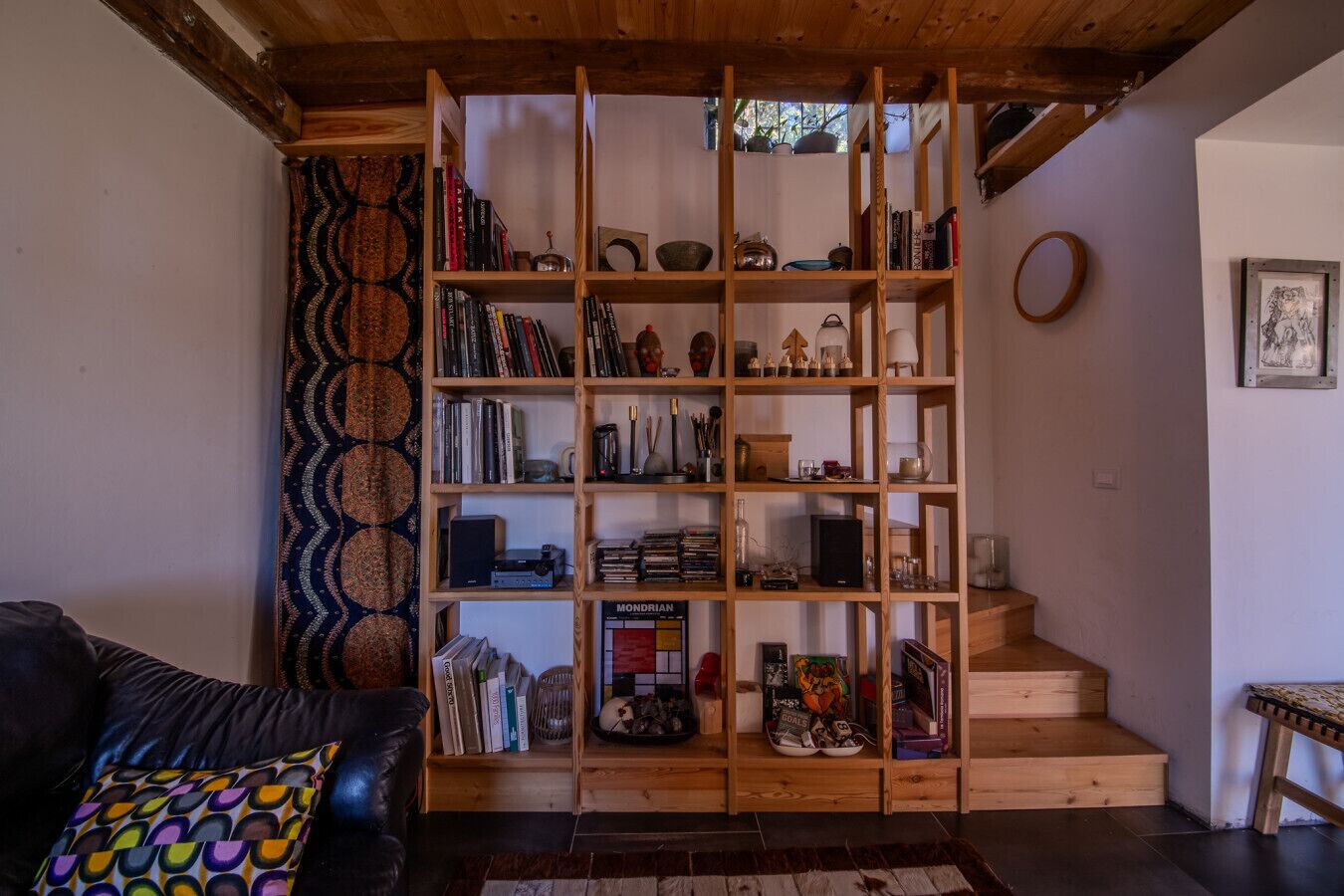 A cozy living room with a wooden bookshelf filled with books, decorative items, and a small table.