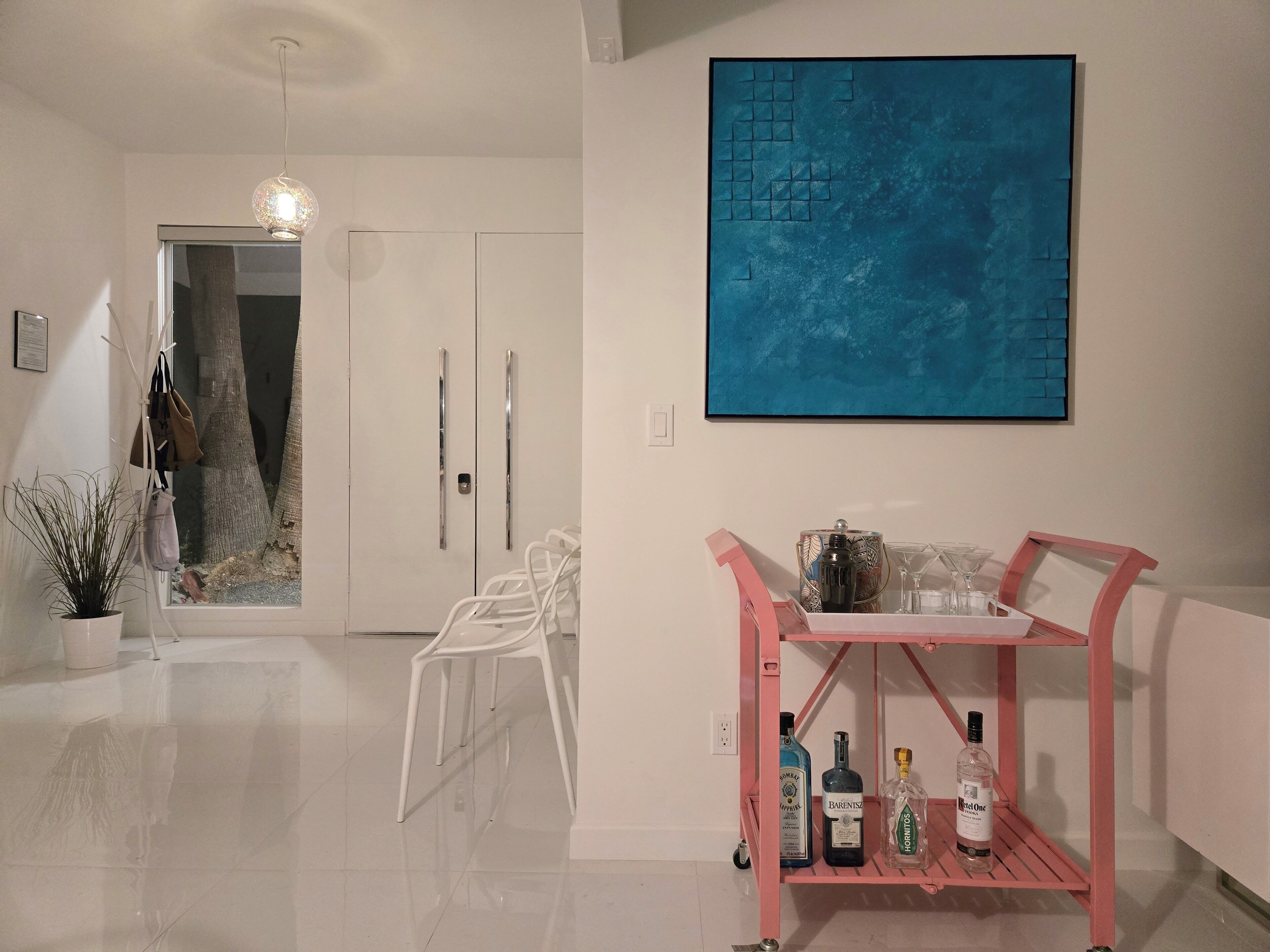 A modern interior with a white door, a blue abstract painting, and a pink shelf with bottles.