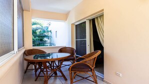Een balkon met een ronde tafel en rieten stoelen, een schuifpui en uitzicht op groen.