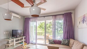 A living room with a TV, glass shelves, a sofa, and a balcony with purple curtains. - Infiniti Blu, Family Suite, Private Beach! (Sosúa)