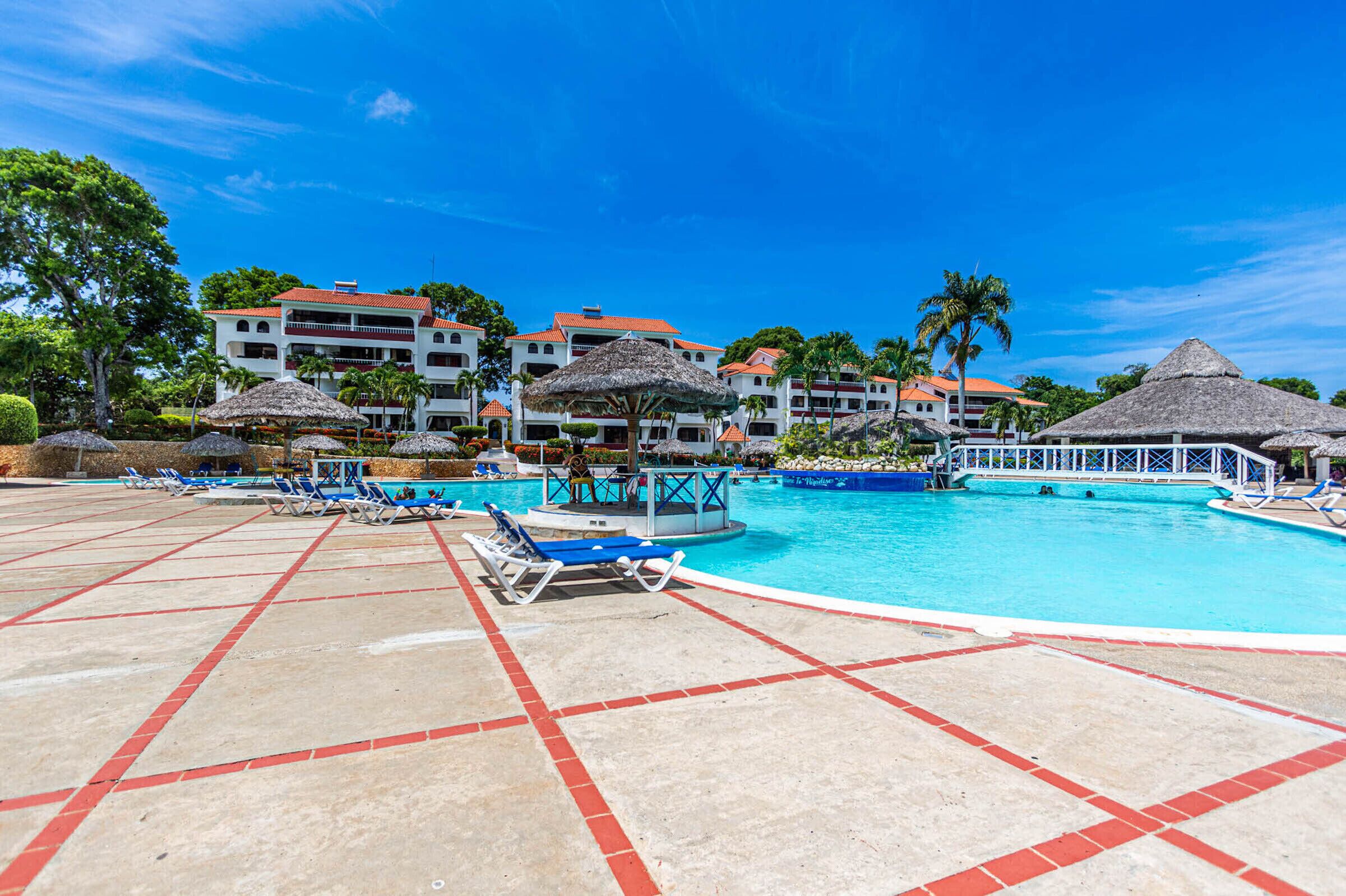 A resort pool area with lounge chairs, umbrellas, and a large swimming pool.