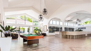 Un espace intérieur spacieux comprenant une table de billard, de grandes fenêtres et un comptoir d’accueil.