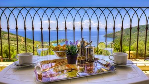 Ein Tisch gedeckt mit Tablett, Tassen, einer Karaffe und einem Glas Wasser, mit Blick auf eine malerische Aussicht auf Meer und Hügel.