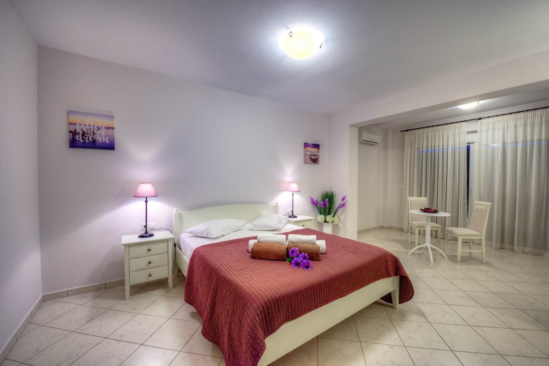Hotelkamer met een bed, bedlampen, een tafeltje met stoelen en uitzicht buiten door een raam met gordijnen.