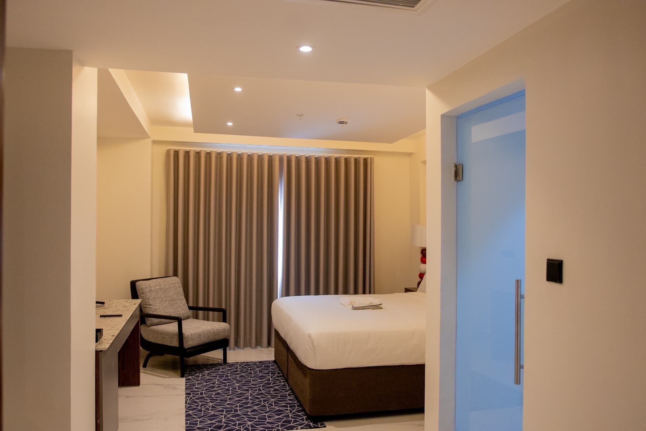 A hotel room with a bed, a desk, a chair, and a window with curtains.