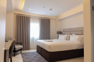A modern hotel room with a large bed, a desk with a chair, and a view of the outdoors through the window.