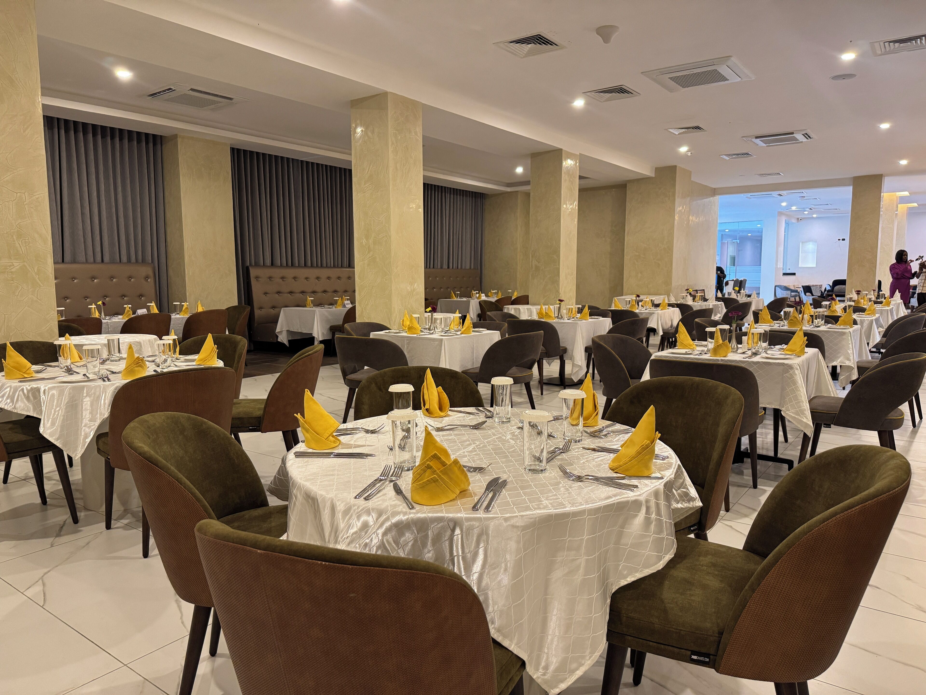 Un vaste espace dédié à la salle à manger, avec des tables rondes, des chaises à revêtement marron et des nappes blanches.