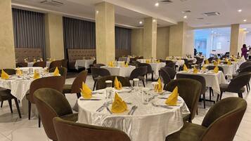 A spacious dining area with round tables, brown upholstered chairs, and white tablecloths.