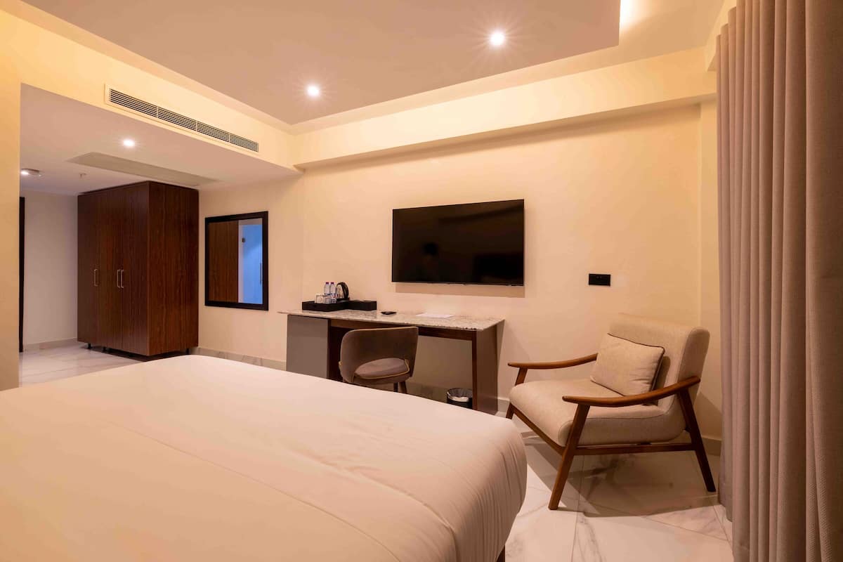 Una habitación de hotel con una cama grande, un escritorio, una silla y un televisor montado en la pared.