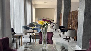 A modern dining area with round tables, purple upholstered chairs, and a central glass table with a vase of flowers. - The Palms by Eagles Airport City (Accra)