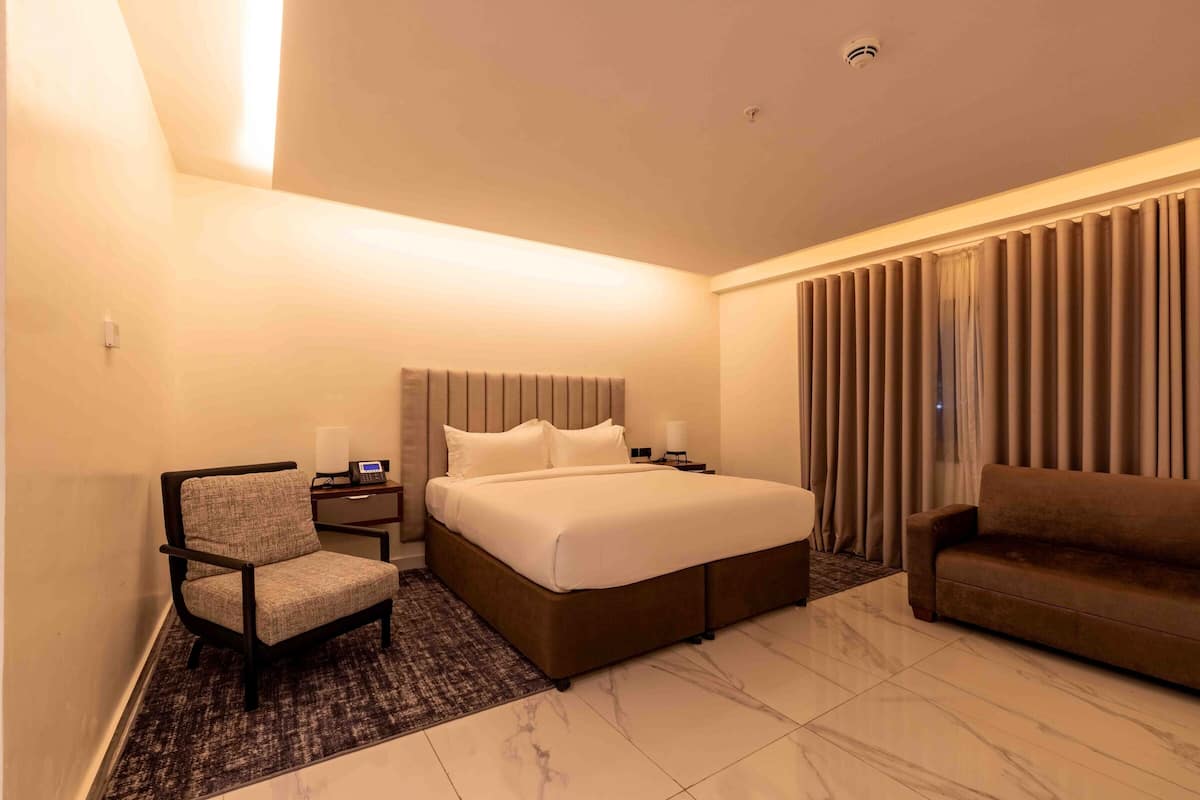 Una habitación de hotel con cama, sillón, sofá, mesita de noche y lámpara.