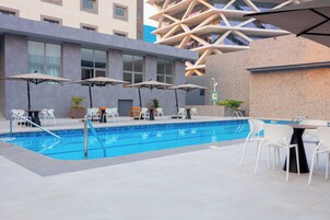 A pool area with a modern pool, white chairs, and umbrellas.