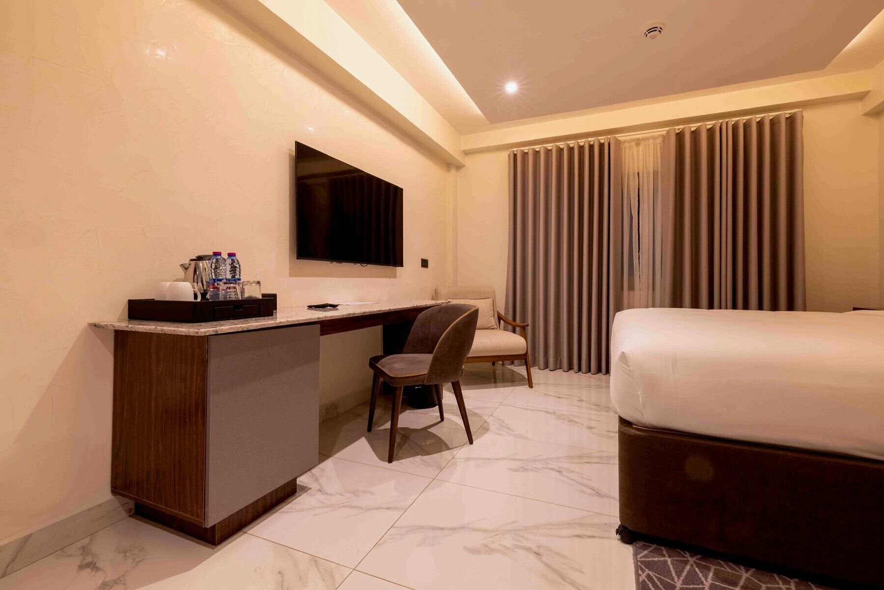 A hotel room with a bed, a desk, a chair, a TV, and curtains.