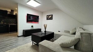 Een moderne woonkamer met een bank, een zwarte salontafel en een aan de muur bevestigde televisie. Op de muur hangt een wereldkaart en op de salontafel staat een kleine plant.