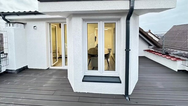 Een wit gebouw met een donker dak, een balkon en een deur naar de binnenruimte.