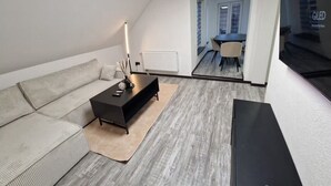 Een moderne woonkamer met een hoekbank, een zwarte salontafel en een flatscreen televisie aan de wand.