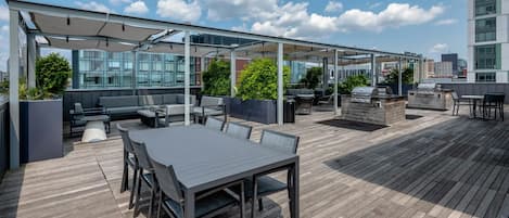 An outdoor patio with a covered seating area, a grill station, and a table with chairs.