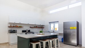 Et moderne køkken med hvide skabe, et rustfrit stål køleskab og en central ø med barstole.