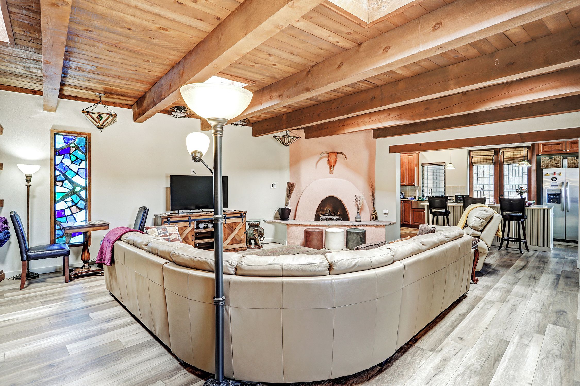 A cozy living room with a large L-shaped sectional sofa, a fireplace, and a kitchen area visible through an open doorway.
