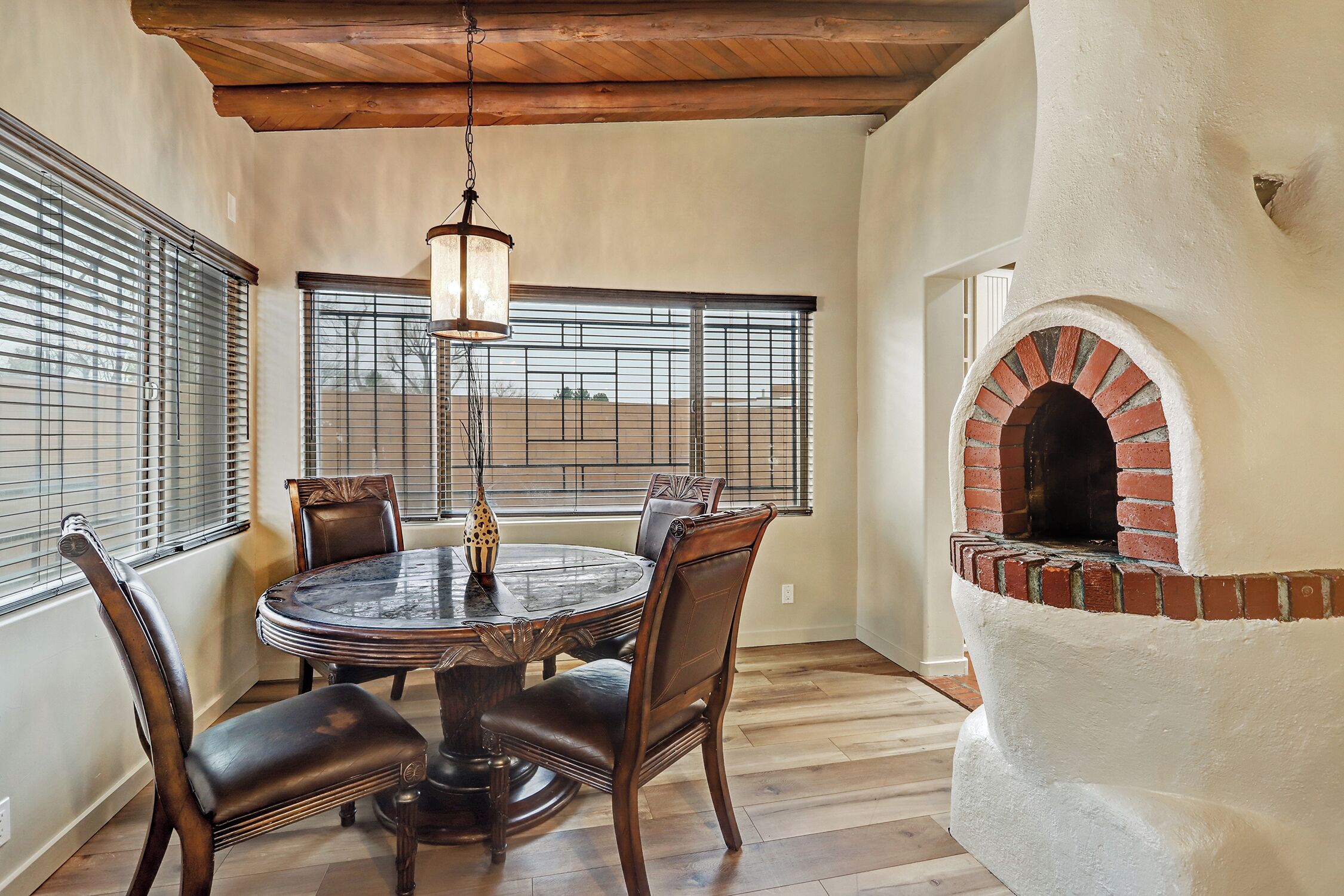 A dining area with a round table and chairs, a hanging light fixture, and a brick oven.