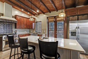 A modern kitchen with a large island, wooden cabinets, stainless steel appliances, and hanging pendant lights. - Spacious Adobe home near Old Town in Albuquerque, New Mexico. (Albuquerque)
