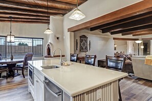 A spacious kitchen with a large island, wooden beams, pendant lighting, and a dining area with chairs and a table. - Spacious Adobe home near Old Town in Albuquerque, New Mexico. (Albuquerque)