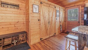 Interior de una cabaña de madera con un banco, una mesa y una puerta con ventanal.