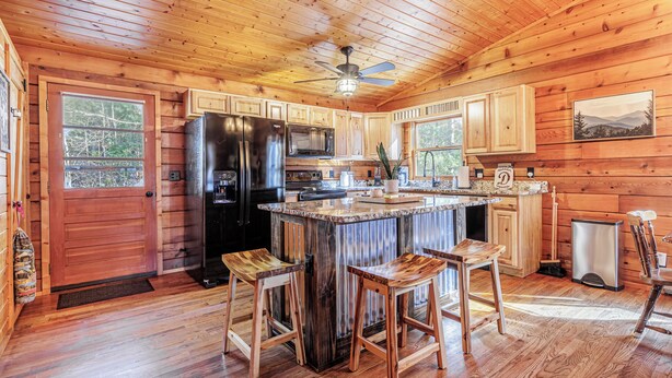 Cocina de cabaña de madera con una isla central, taburetes de bar, refrigerador, microondas y ventilador de techo.