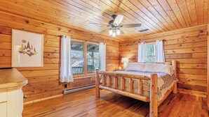 Un dormitorio de cabaña de madera con una cama, un ventilador de techo y una ventana con cortinas.