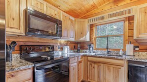 Cocina moderna con armarios de madera, electrodomésticos de acero inoxidable, encimeras de granito y un amplio ventanal que proporciona luz natural.