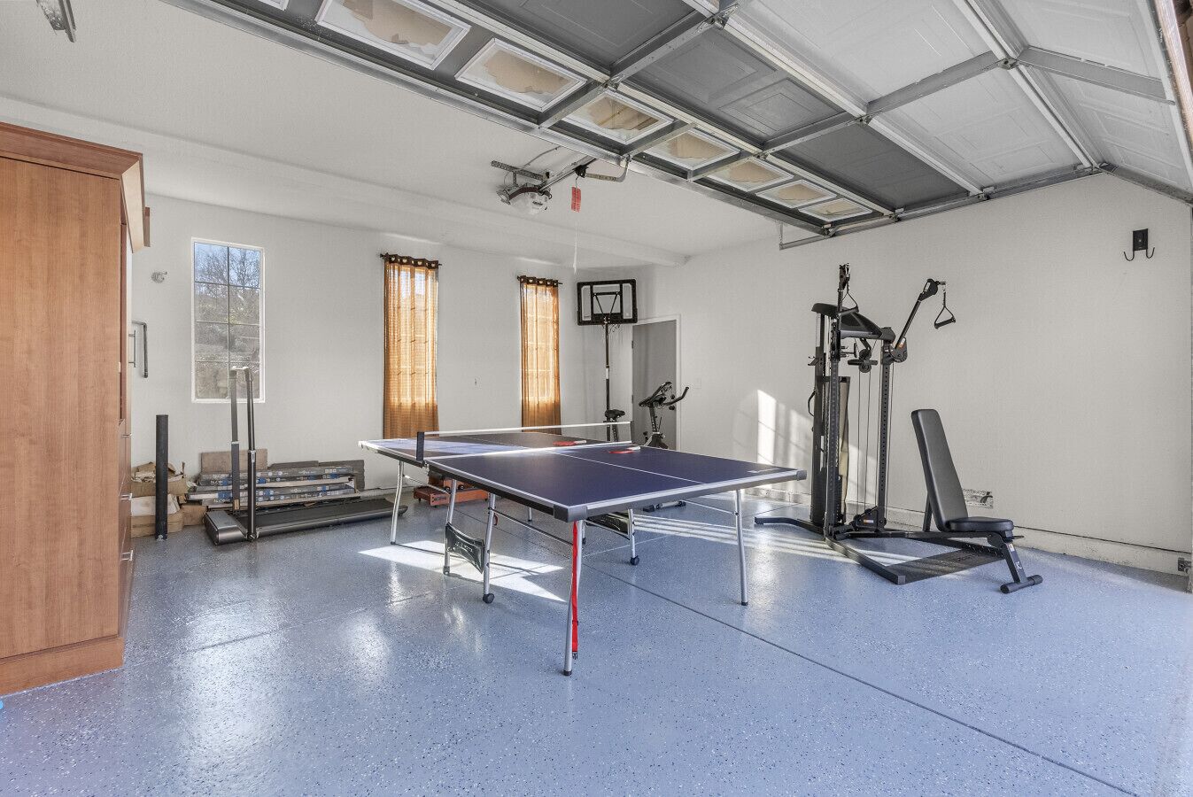 Un amplio espacio interior con mesa de ping pong, equipo de ejercicio y una puerta.