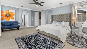 A bedroom with a large bed, a ceiling fan, a blue sofa, and a painting of a flower. - Game Lovers` Retreat: 4000 sqft of Fun (El Dorado Hills)