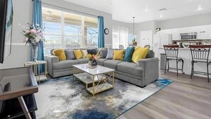 A modern living room with a grey sofa, a coffee table, and a dining area with a bar. - Spacious 7-Bedroom Private Pool, Minutes From Disney (Kissimmee)