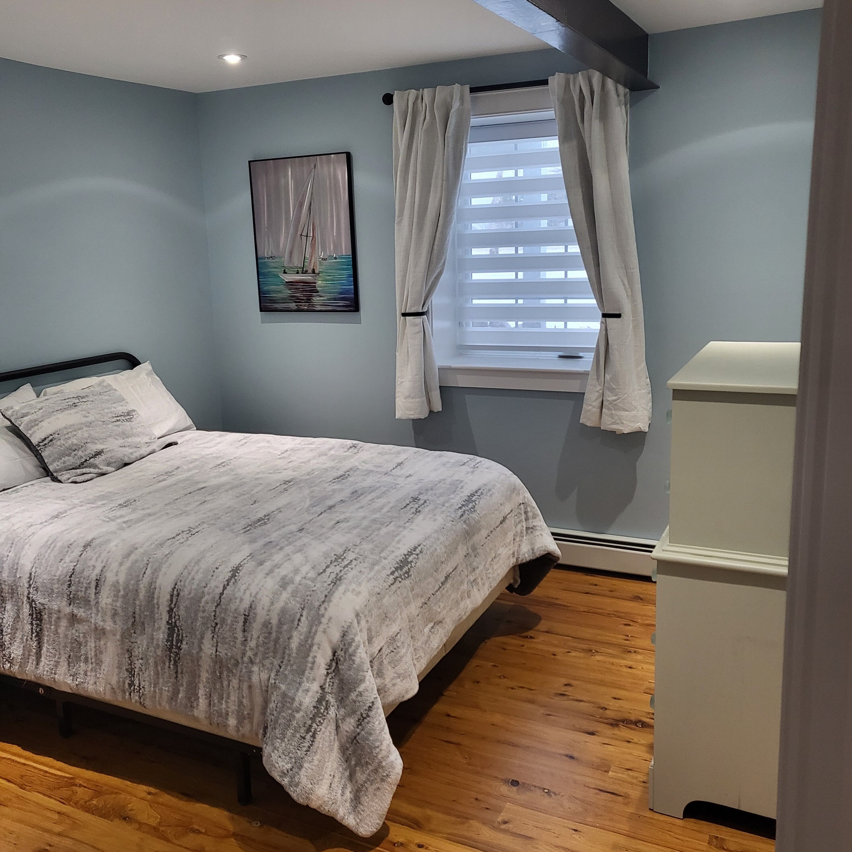 Un dormitorio con cama, ventana con cortinas, un cuadro en la pared y un armario blanco.